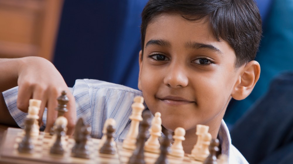 A smiling ElementX student thinking through his next chess move